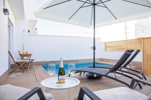 A poolside area with a table, lounge chairs, and a bottle of wine. - Luxury Holiday Home Berlin - San Pedro del Pinatar (San Pedro del Pinatar)