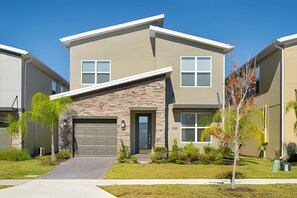 A modern two-story townhouse with a stone facade, a garage, and a well-maintained front yard with landscaping. - 5BR Home w/ Pool, Game Room + Near Disney (Davenport)