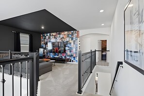 A modern interior with a staircase, a wall of books, and a minimalist design. - 5BR Home w/ Pool, Game Room + Near Disney (Davenport)