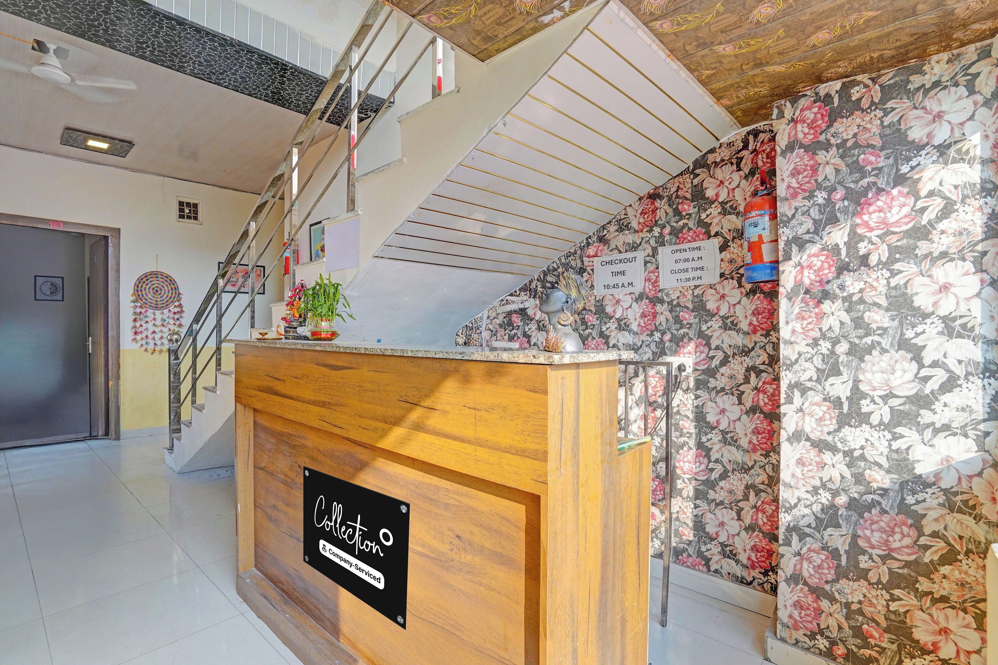 Zona de recepción de un hotel con mostrador de madera, una escalera y papel tapiz floral.