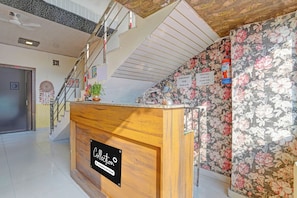 A hotel reception area with a wooden counter, a staircase, and floral wallpaper. - Collection O Meerut City Junction (Meerut)