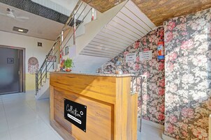 A hotel reception area with a wooden counter, a staircase, and floral wallpaper.