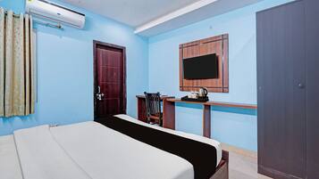 Habitación de hotel con cama, escritorio con silla, televisor en la pared y armario.