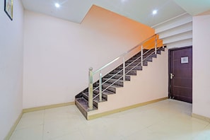 Escadaria com corrimão de metal e acabamento em mármore escuro, levando a uma porta com uma placa acima.