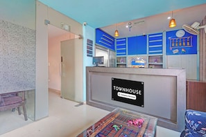 Uma área de recepção com placa indicando ser uma townhouse de serviço da empresa. Há um balcão de recepção, um relógio e uma parede com detalhes decorativos, incluindo bandeiras.