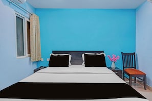 Una habitació amb un llit, una cadira, una taula de nit, un ram de flors i una finestra amb cortines.