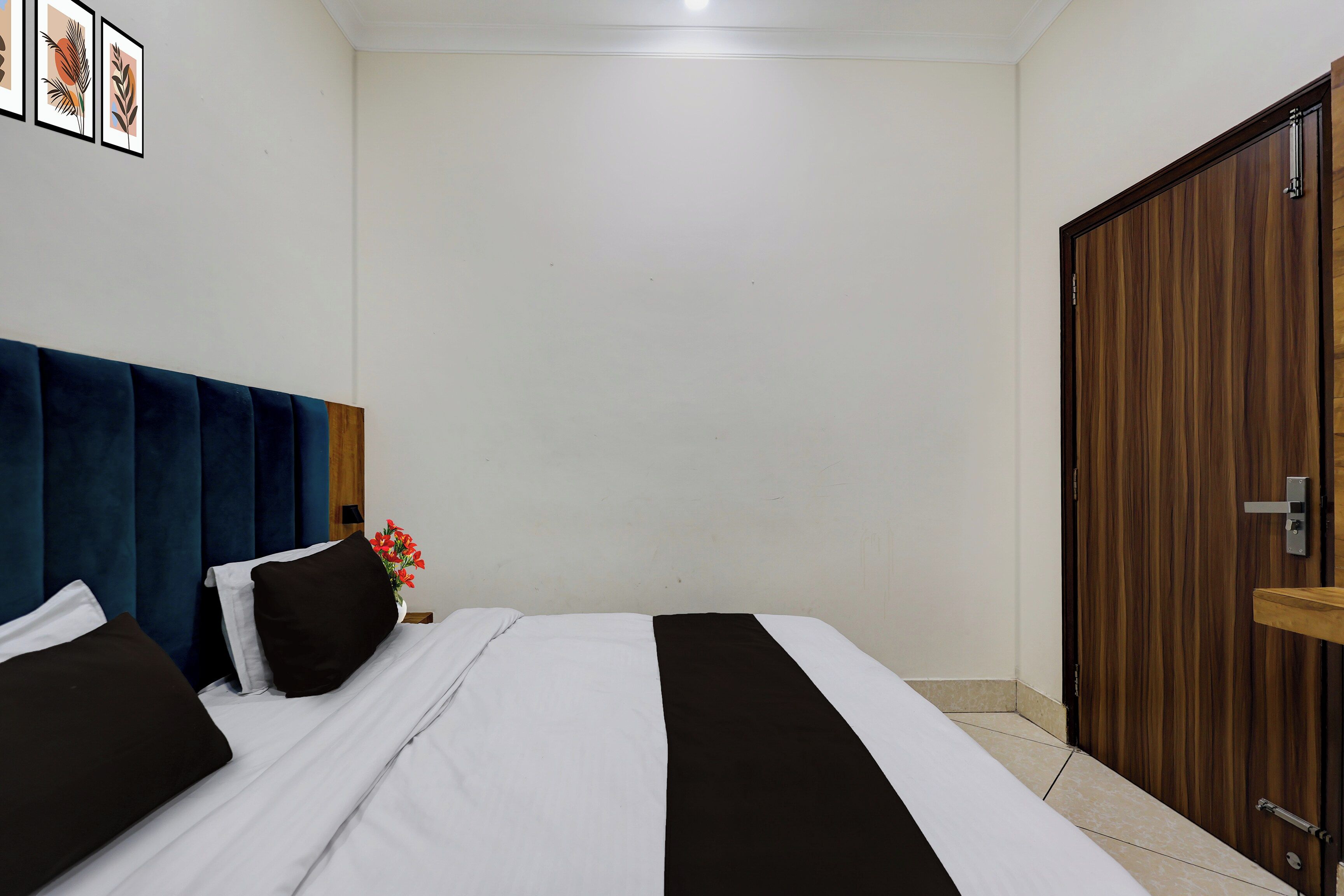 A hotel room with a bed, a wooden wardrobe, and a wall with framed artwork.
