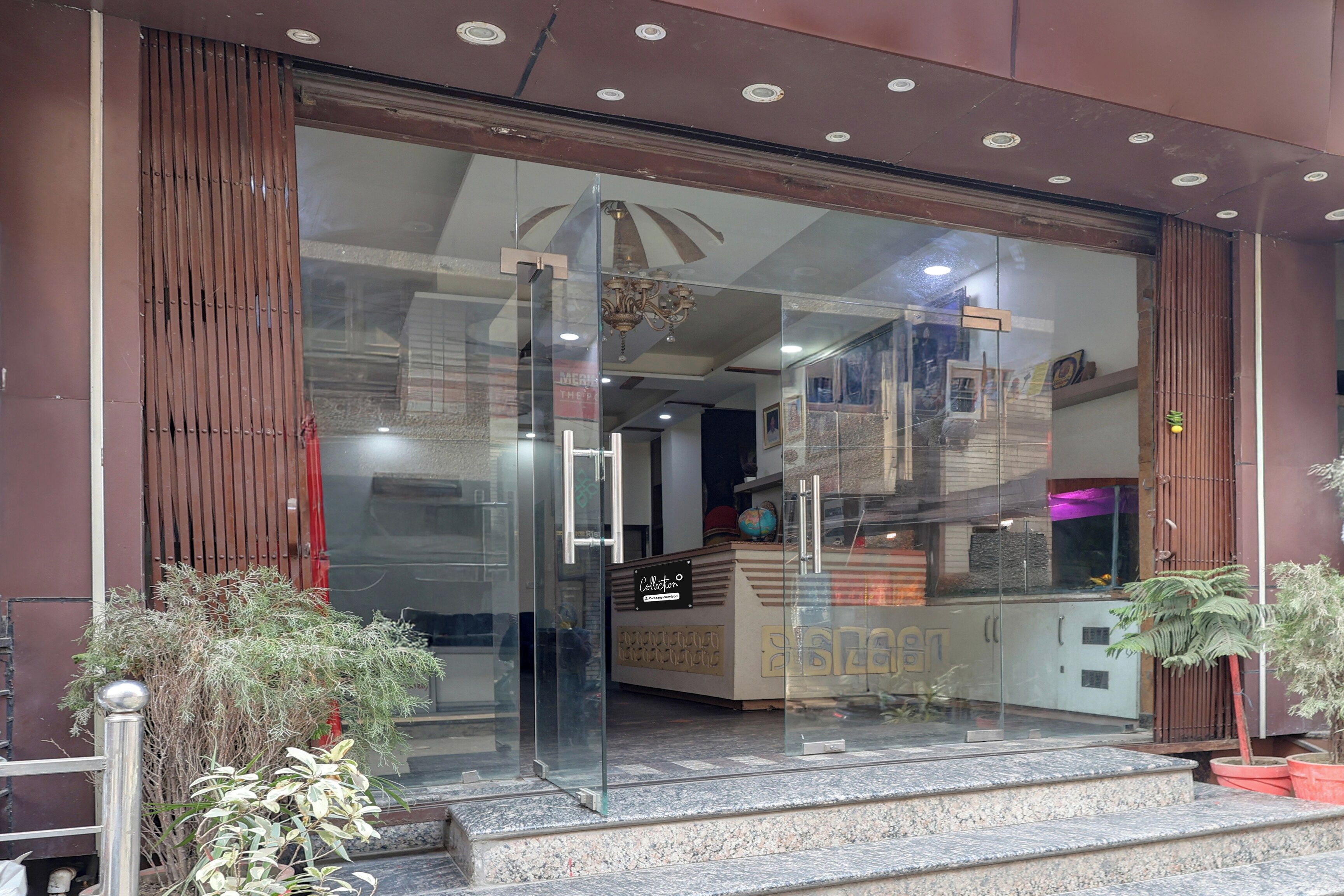A hotel entrance with a glass door, a reception desk, and a staircase leading inside.