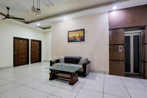 Una habitación con una mesa de centro de vidrio, un sofá, un ventilador de techo y un cuadro en la pared.