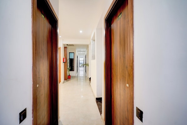 A corridor with wooden doors, a fire extinguisher, and a potted plant. - Townhouse Sector 67A Gurgaon (Sohna)