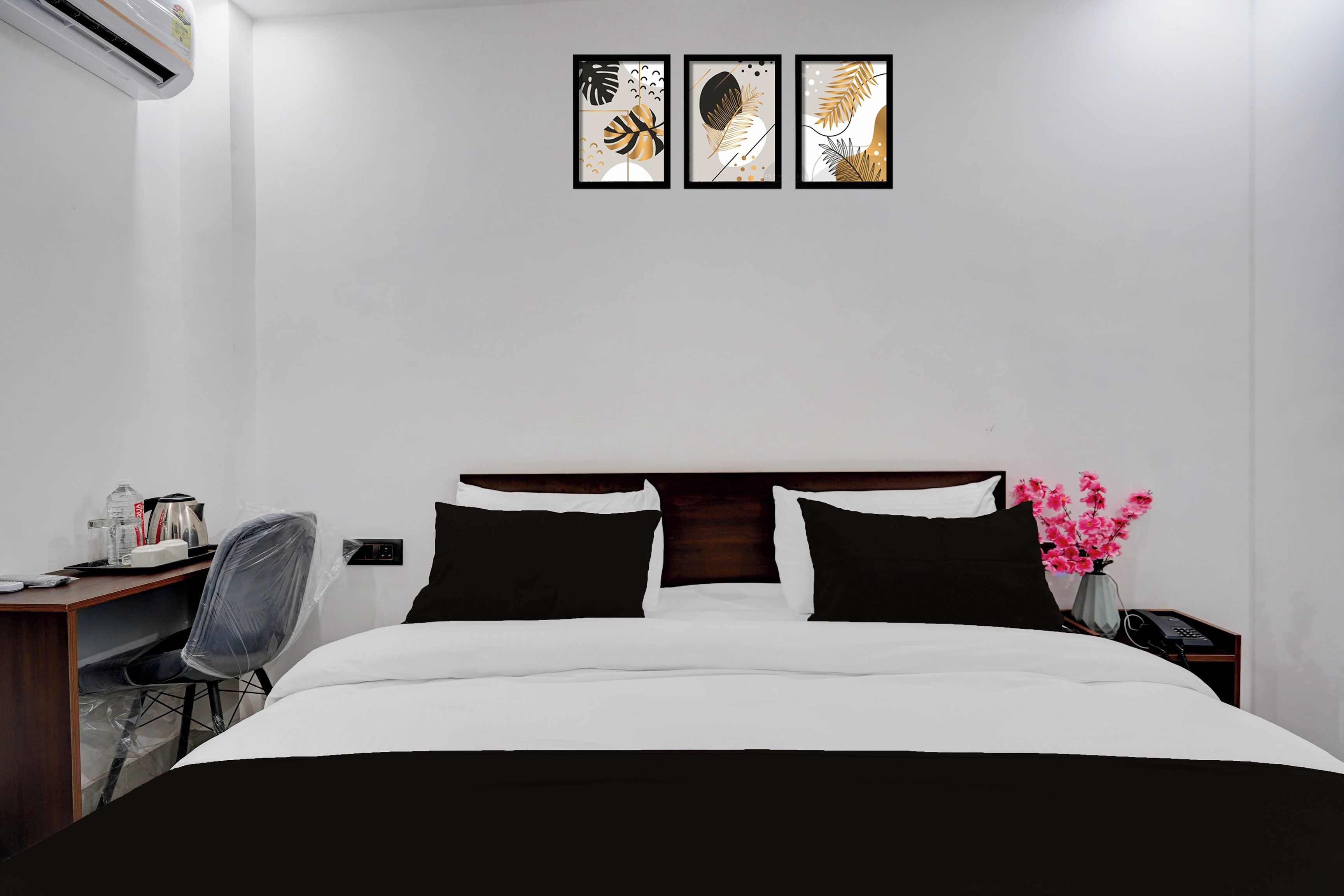 Ein Hotelzimmer mit Bett, Schreibtisch, Stuhl, Nachttisch, einer Vase mit Blumen und Bildern an der Wand.