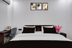 Una habitación de hotel con una cama, un escritorio, una silla, una mesita de noche, un jarrón con flores y obras de arte en la pared.
