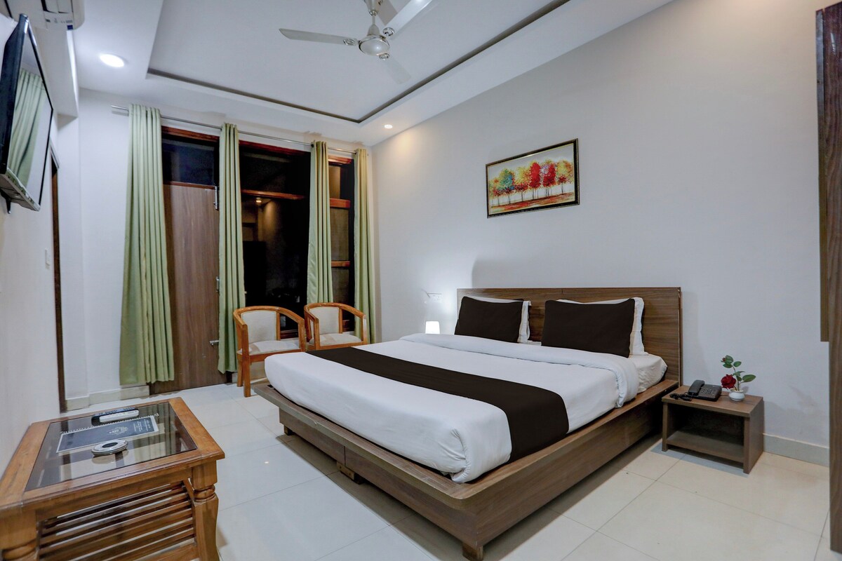 A hotel room with a bed, a desk, a chair, a nightstand, a painting, and a ceiling fan.