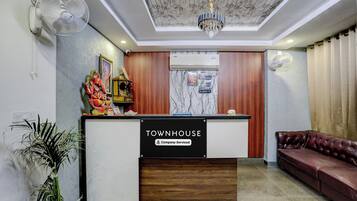 Ein Empfangstresen mit dem Schild 'TOWNHOUSE Company-Serviced', ein Deckenventilator, eine Kristallleuchter, ein braunes Ledersofa und ein Topfpflanze.