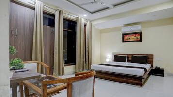 A hotel room with a bed, a desk with a chair, a window with curtains, a ceiling fan, and an air conditioning unit.
