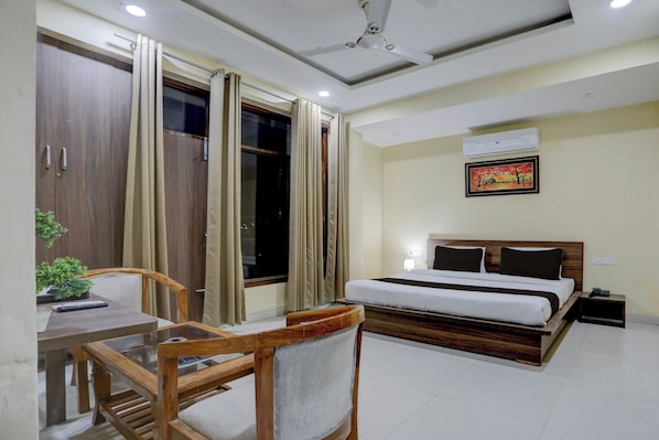 A hotel room with a bed, a desk with a chair, a window with curtains, a ceiling fan, and an air conditioning unit.