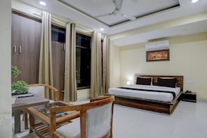 Una habitación de hotel con cama, escritorio con silla, ventana con cortinas, ventilador de techo y aire acondicionado.
