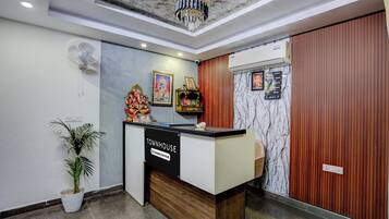 A reception desk with a sign indicating it is a company-serviced area, a ceiling fan, a potted plant, and a marble-patterned wall.