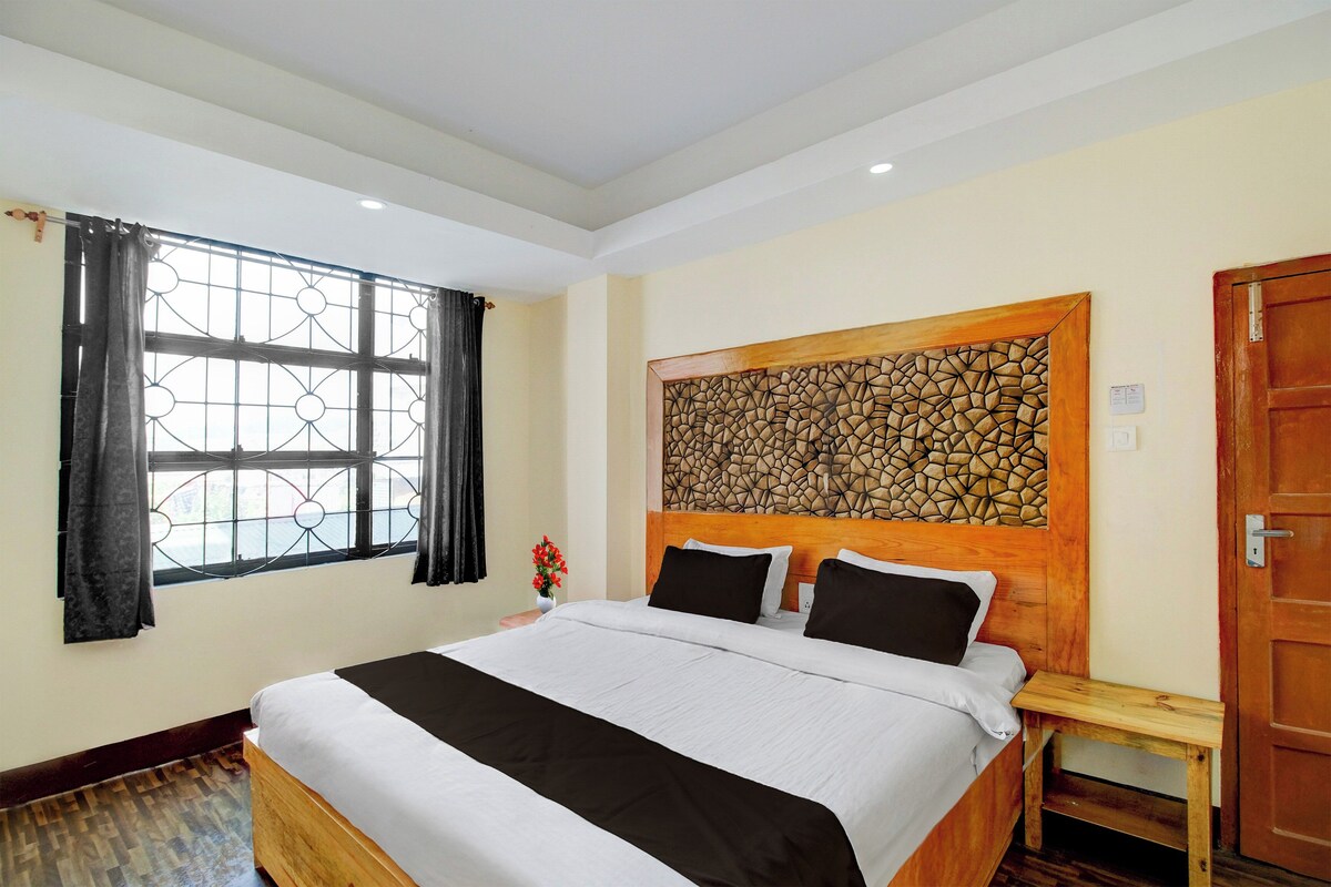 A hotel room with a large bed, a window with curtains, a wooden headboard, and a door.