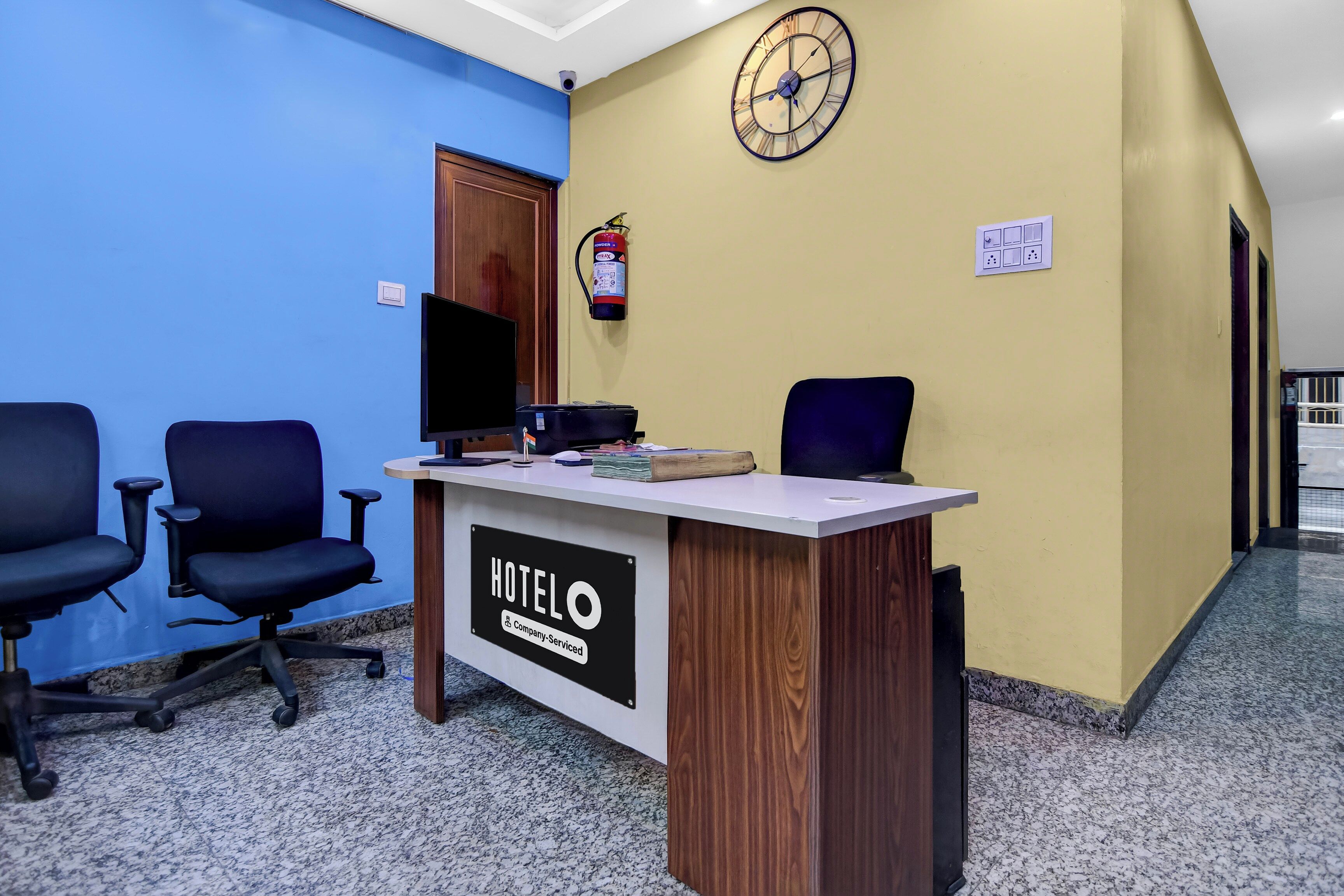 Un comptoir de réception d’hôtel avec une horloge, un extincteur et un panneau indiquant qu’il est entretenu par l’entreprise.