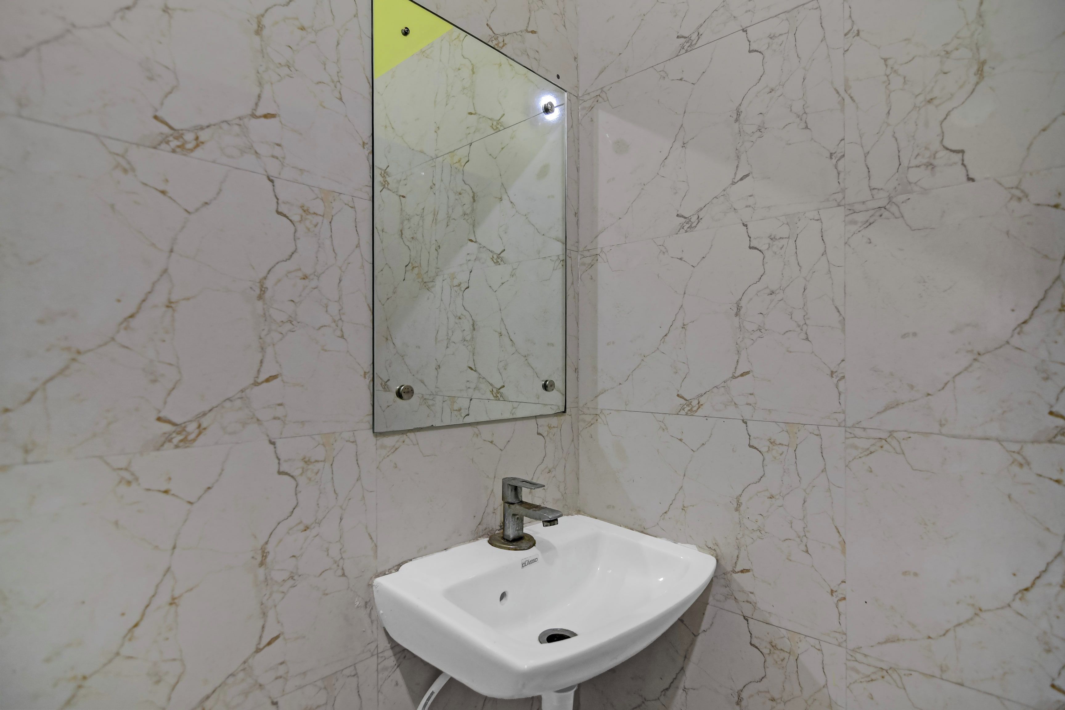 A bathroom with a white marble wall, a white sink, and a mirror.