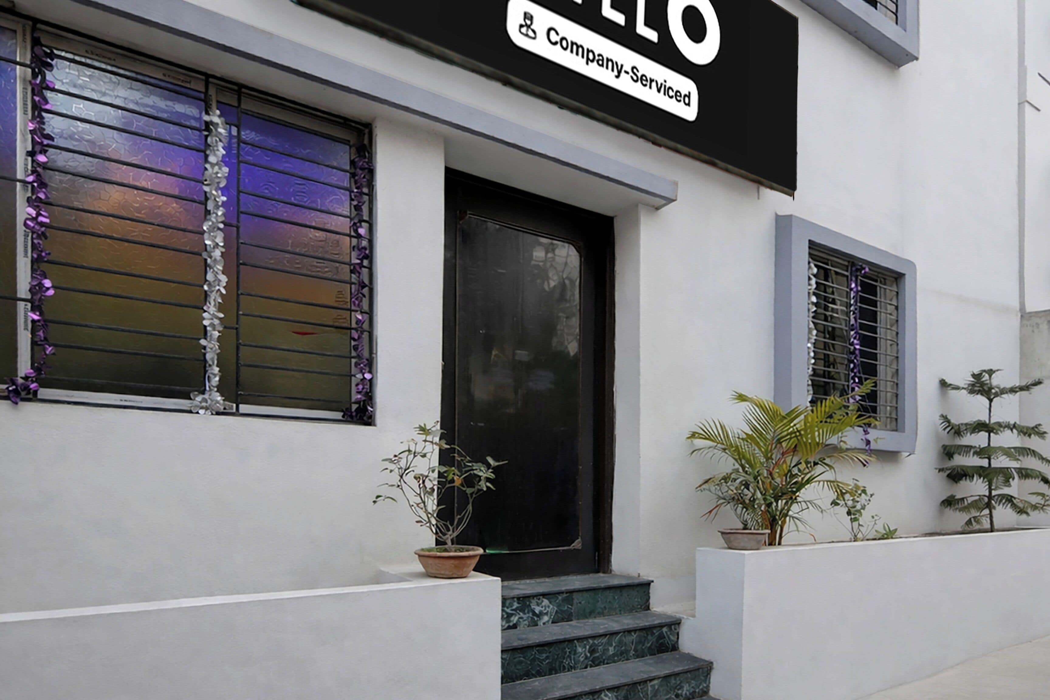 Un edificio con una puerta negra, una ventana con detalles decorativos morados y un letrero que dice 'Company Serviced'.