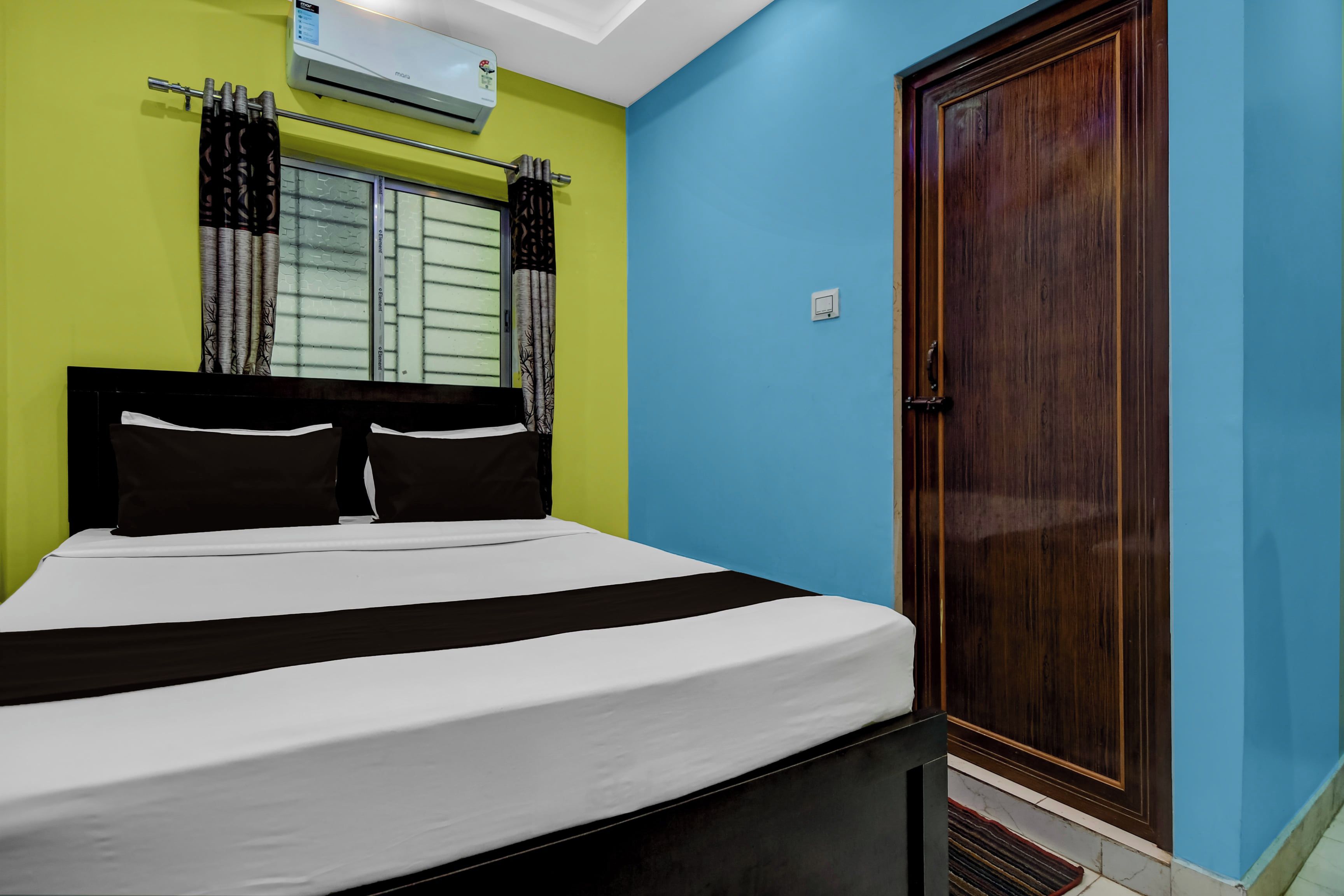 Un dormitorio con cama, cortinas, una ventana, un equipo de aire acondicionado y una puerta de madera.