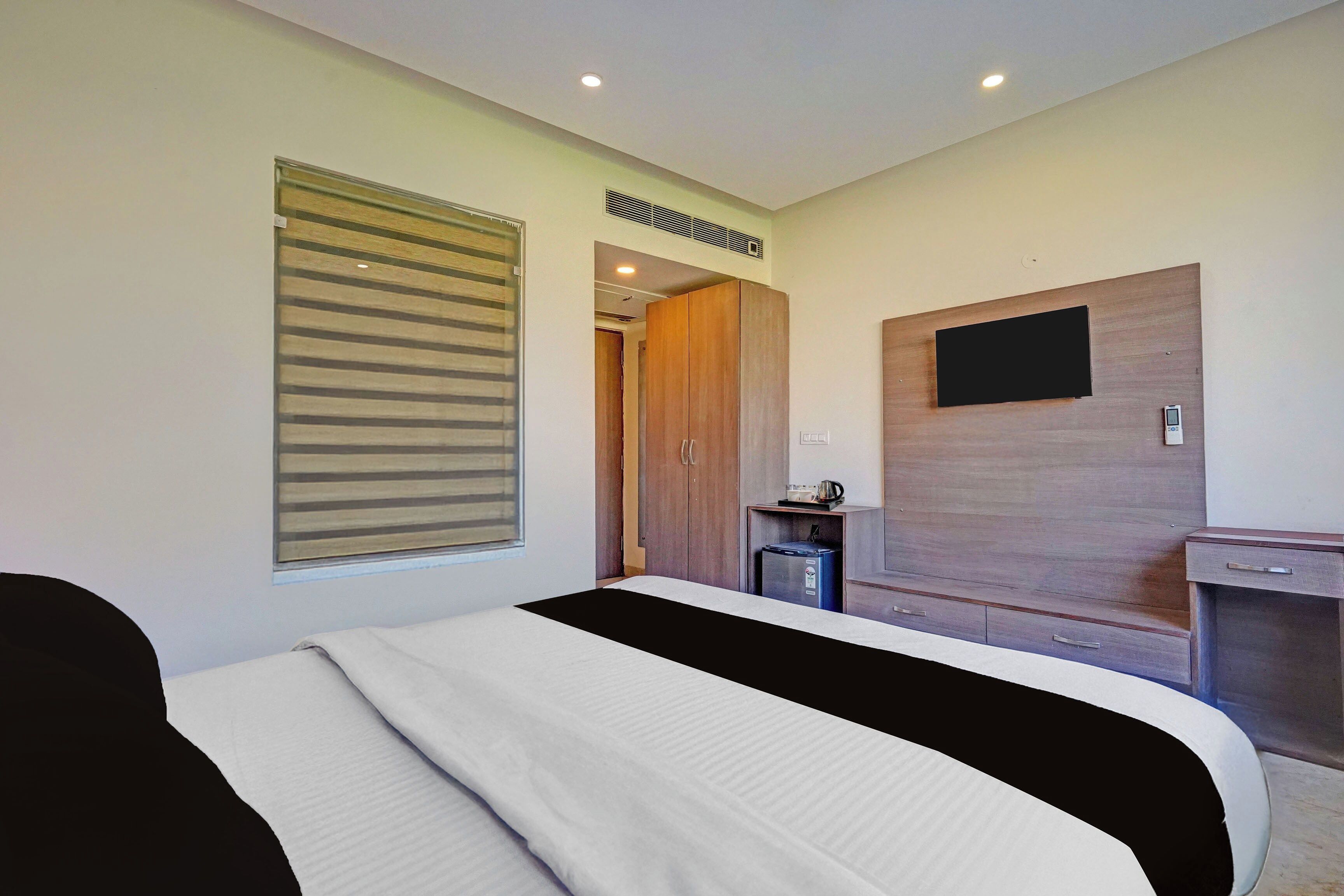 Una habitación de hotel con cama, escritorio, televisor y ventana con persianas.