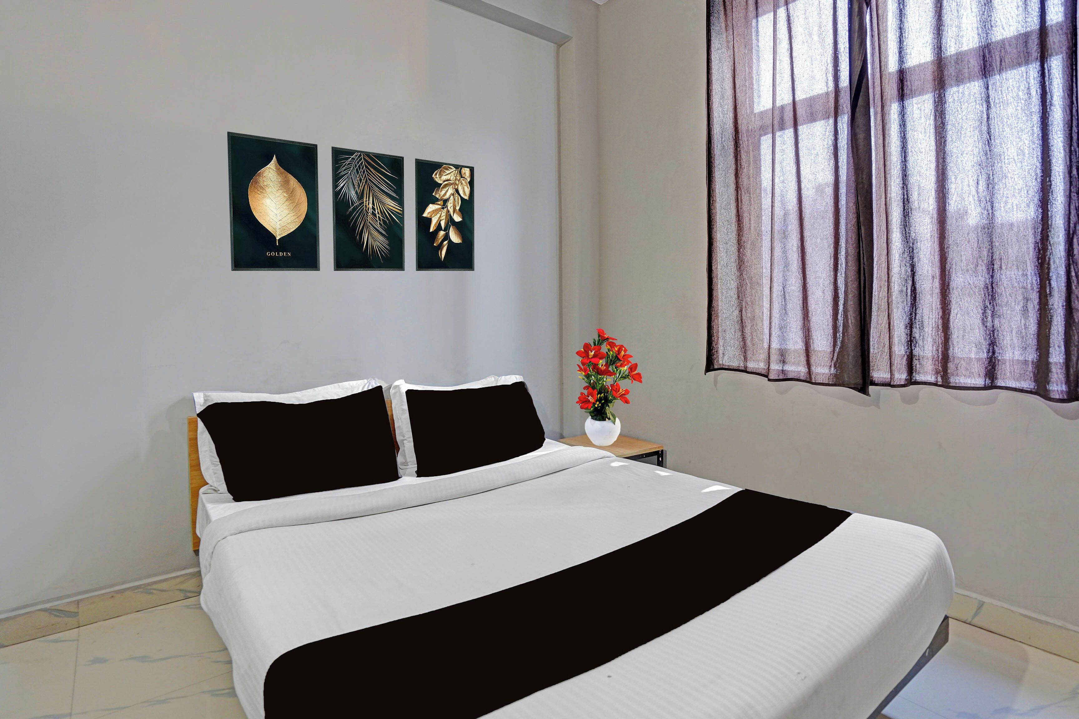 Une chambre à coucher avec un lit, une table de chevet ornée d’un vase de fleurs et trois motifs de feuilles encadrés accrochés au mur.