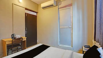 Habitación de hotel con cama, escritorio con hervidor, silla, puerta y equipo de aire acondicionado.
