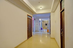 Corredor de hotel com piso de azulejos, portas de madeira e luminária no teto.