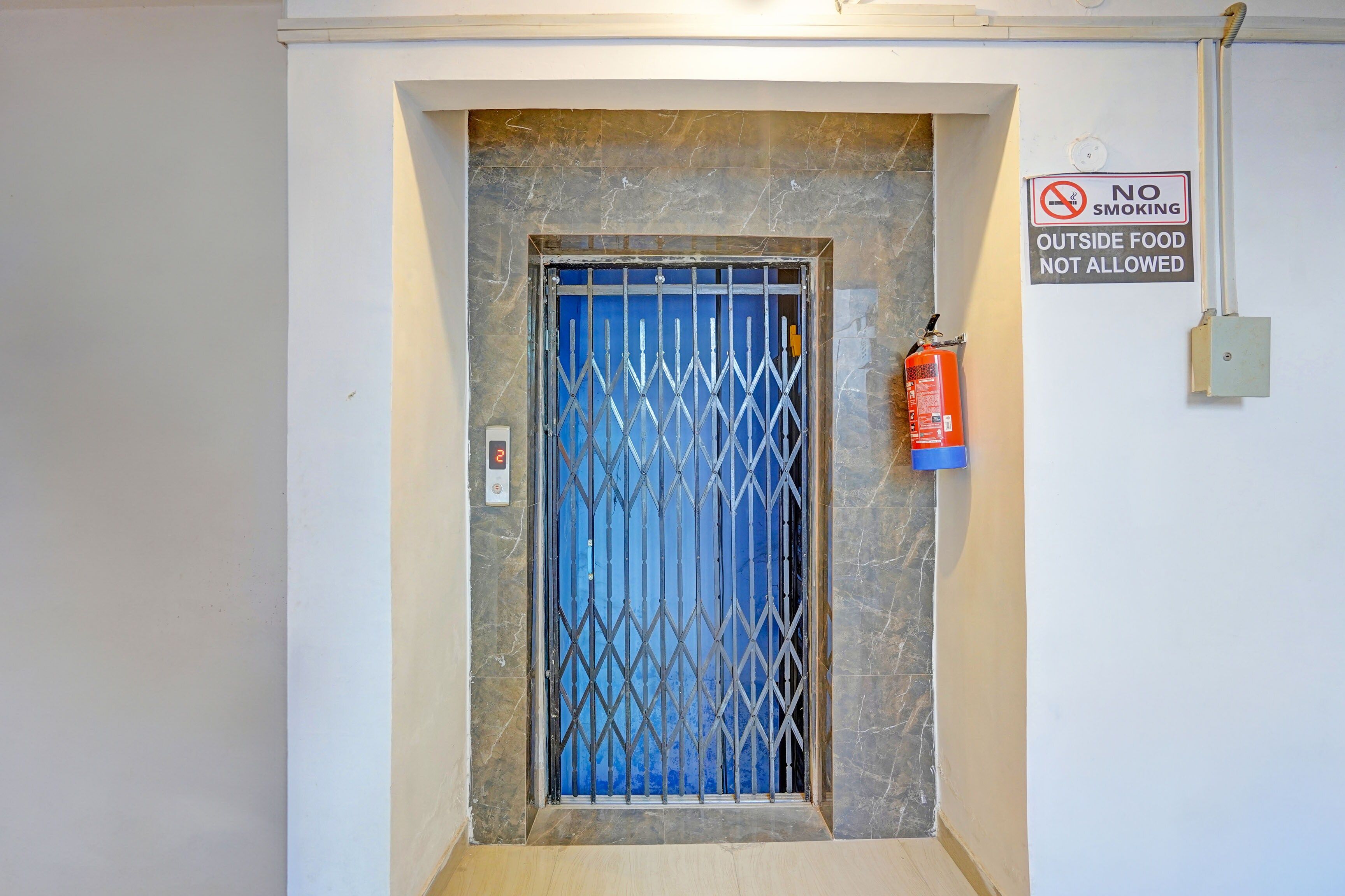 Una puerta con una reja de metal, un extintor en la pared y un cartel de 'NO FUMAR'.