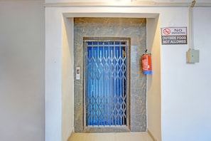 Uma porta com portão de metal, um extintor fixado na parede e um aviso de 'PROIBIDO FUMAR'.