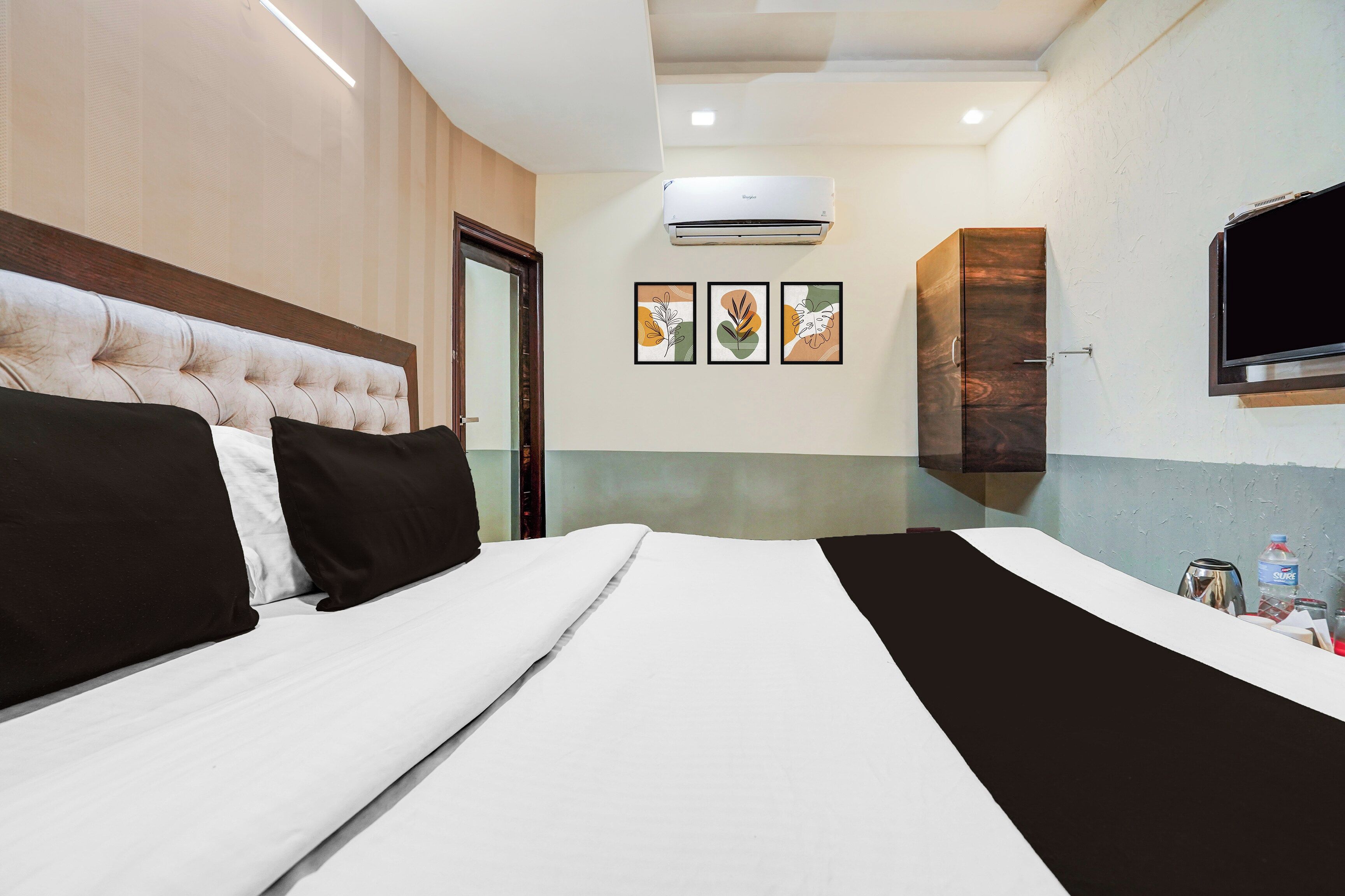 A hotel room with a large bed, a flat-screen TV mounted on the wall, and a ceiling air conditioner.