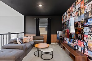 Ett modernt vardagsrum med en grå soffa, ett runt soffbord och en vägg som är dekorerad med en fotokollage.