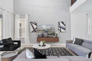 Ein modernes Wohnzimmer mit einem grauen Sofa, einem schwarz-weißen Teppich und einem Couchtisch mit Dekorationselementen.