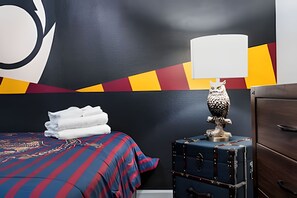 Ett hotellrum med en säng, en lampa, en byrå och en vägg med ett geometriskt mönster.
