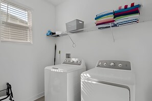 A laundry room with two white washing machines, a drying rack with colorful towels, and a window with blinds. - 6BR Disney-themed Villa + Pool & Game Room (Kissimmee)