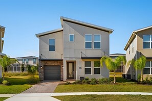 A modern two-story residential building with a garage, large windows, and a well-maintained lawn. - 6BR Disney-themed Villa + Pool & Game Room (Kissimmee)