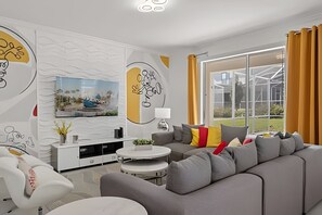 A modern living room with a grey sofa, white entertainment unit, and a large window with curtains. - 6BR Disney-themed Villa + Pool & Game Room (Kissimmee)
