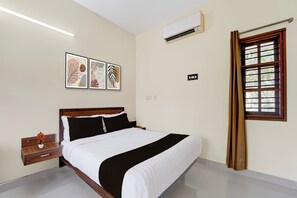 A hotel room with a bed, a nightstand, a vase with flowers, a window with curtains, and wall-mounted air conditioning.