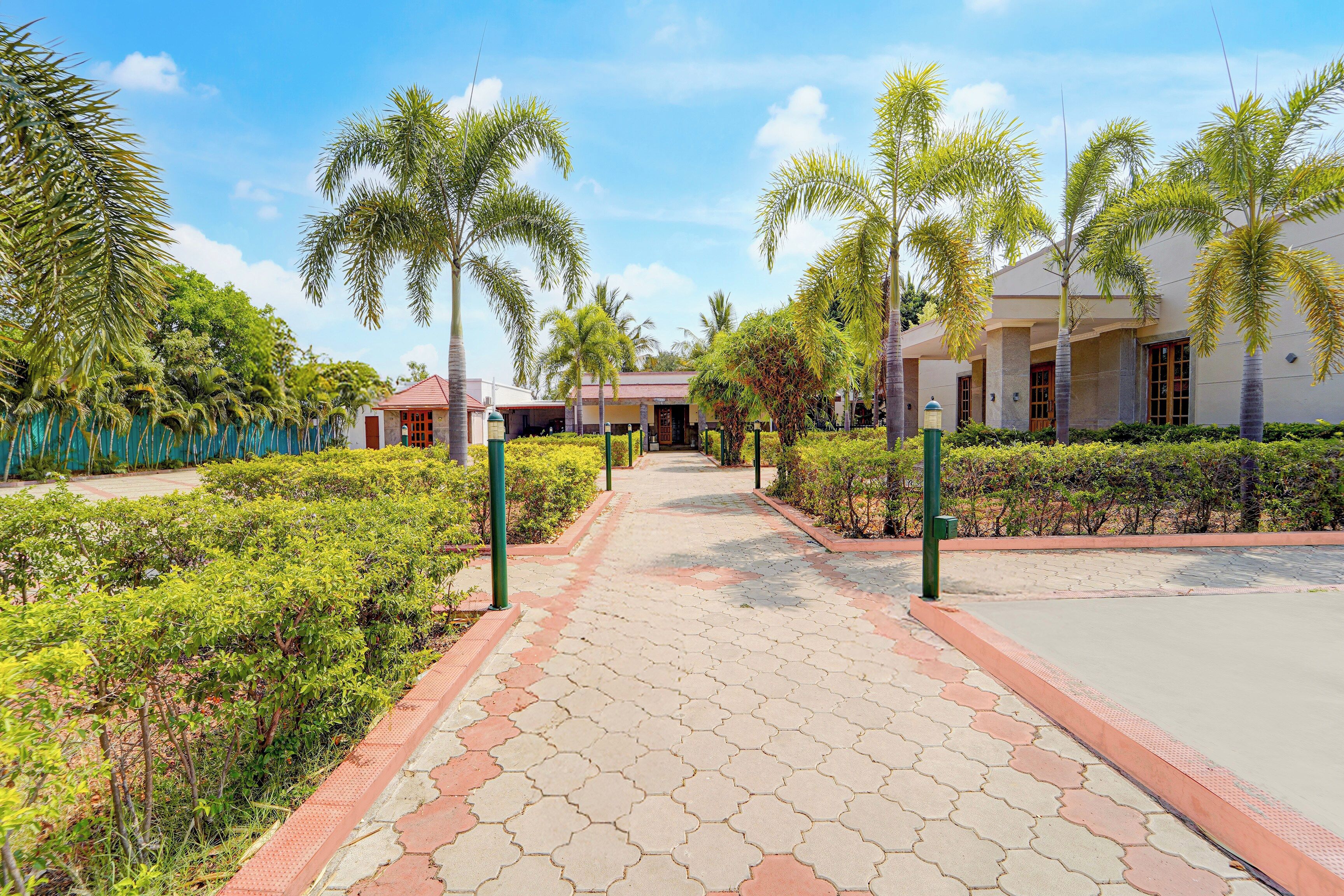 A pathway leading to a building with a red roof, surrounded by greenery and palm trees.