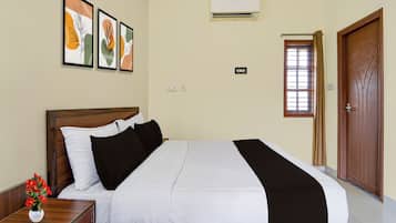 Habitación de hotel con cama, mesita de noche, un jarrón de flores, ventana con persianas y puerta.