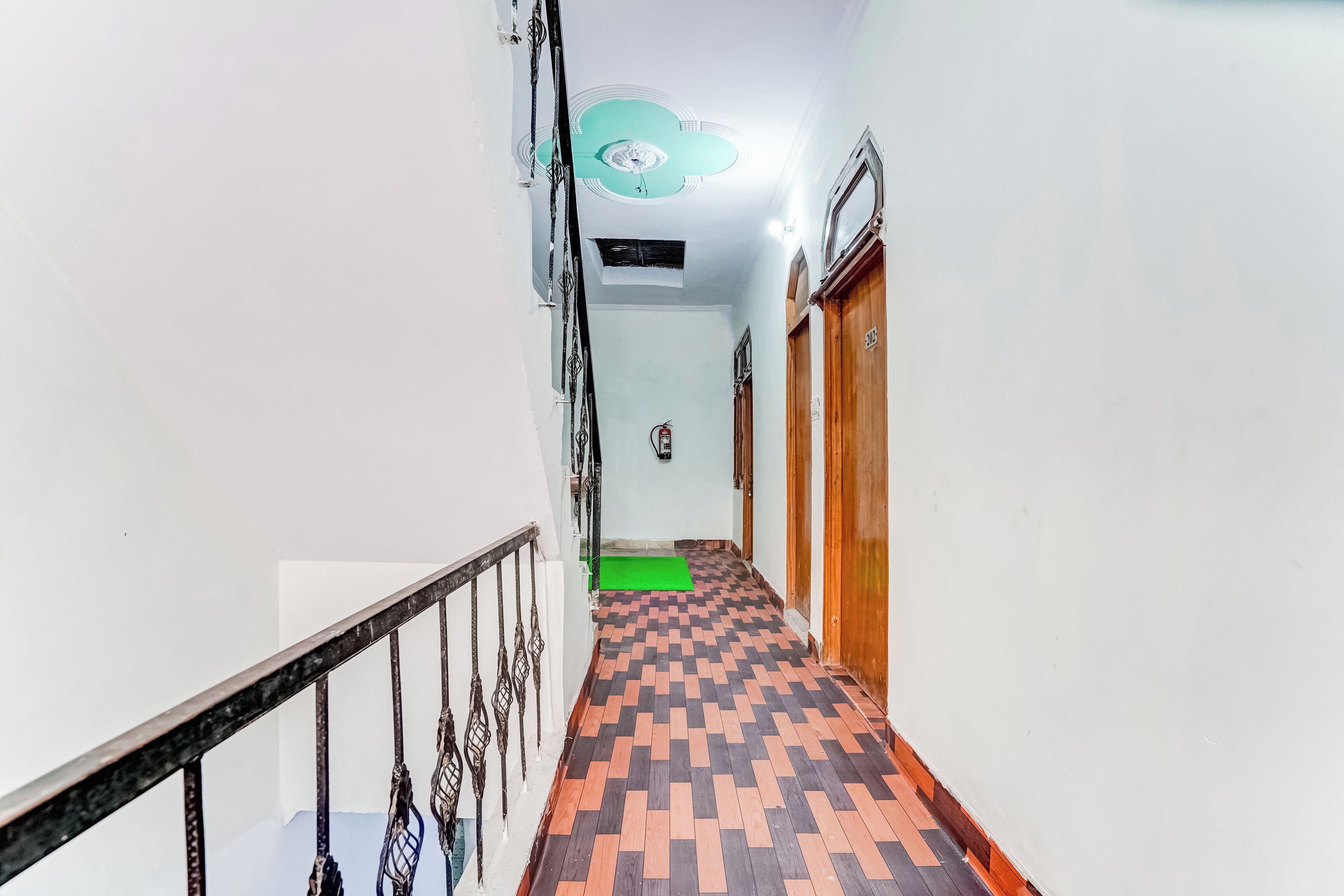 A corridor with a patterned floor, a metal railing, and a ceiling with a circular light fixture.