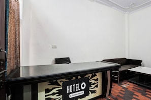 A hotel reception desk with a sign indicating it is company-serviced. There are two chairs and a sofa in the room. - Hotel O Sector 12 Ghaziabad (Ghaziabad)