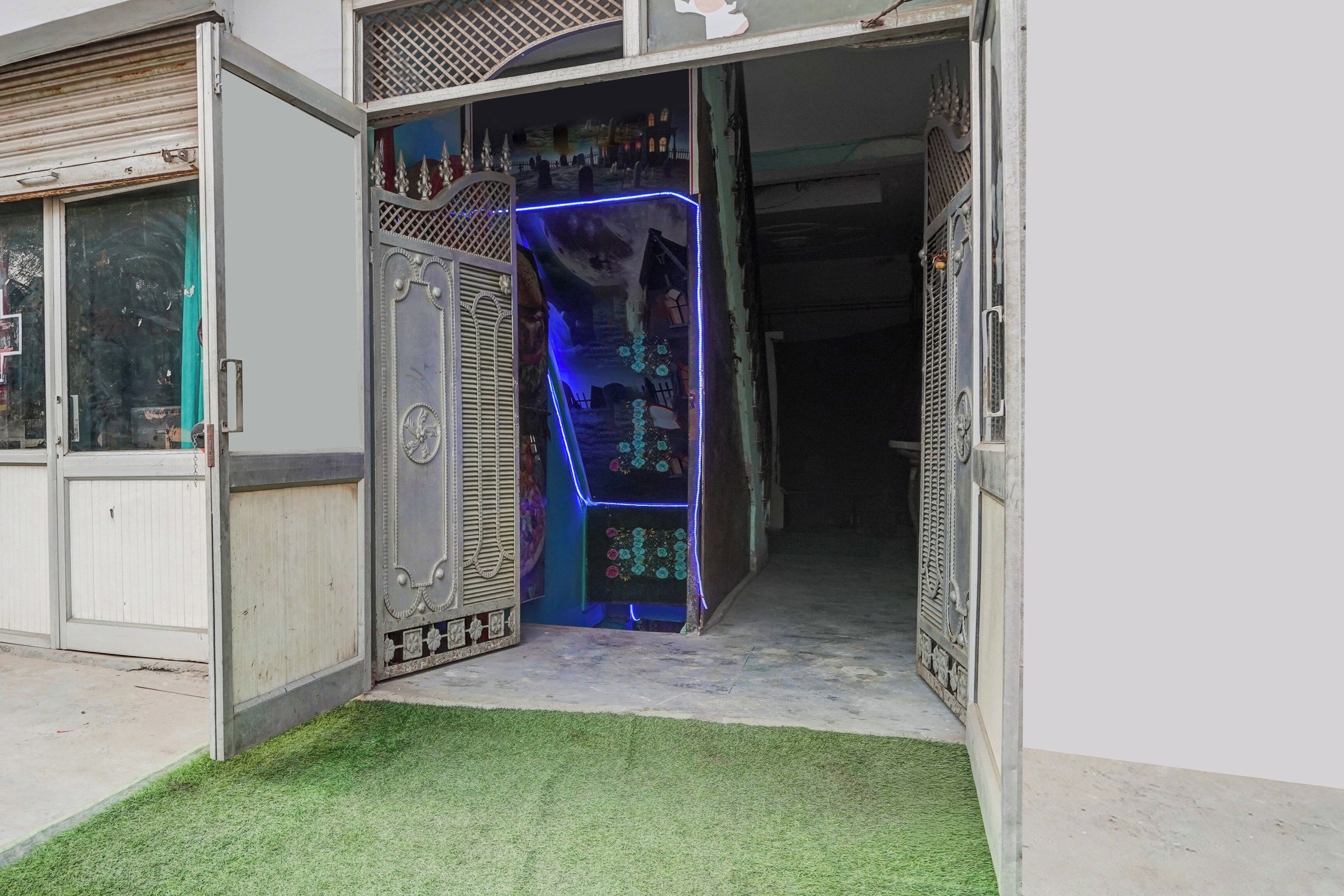 A building entrance with a decorative metal gate, a small grassy area, and a blue-lit structure inside.