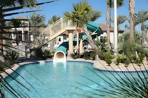 A swimming pool with a slide, palm trees, and a building with a balcony. - Disney Area Championsgate 4BR Townhome w/ Pool (Davenport)