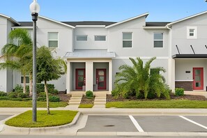 A modern multi-story residential building with a central entrance, a covered porch, and a parking area in front. - Disney Area Championsgate 4BR Townhome w/ Pool (Davenport)