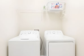 Two front-loading washing machines with control panels, a clear shelf above them, and a white wall. - 6BR Villa w/ Pool & Game Room Near Disney (Davenport)