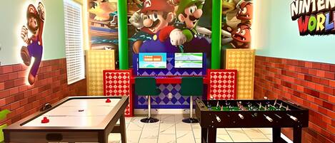A room with a foosball table, a pool table, and a Mario-themed mural.
